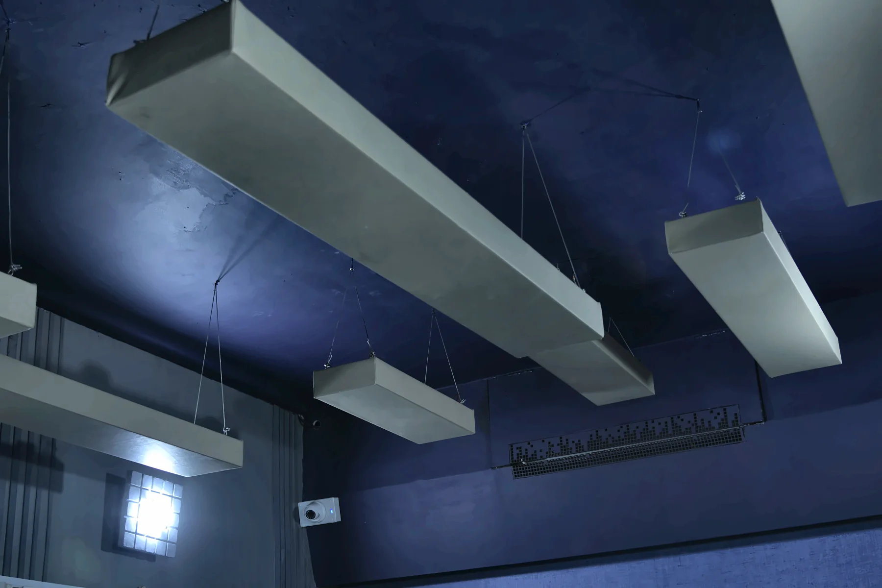 The ceiling and wall in blue light, panels hanging over the room.