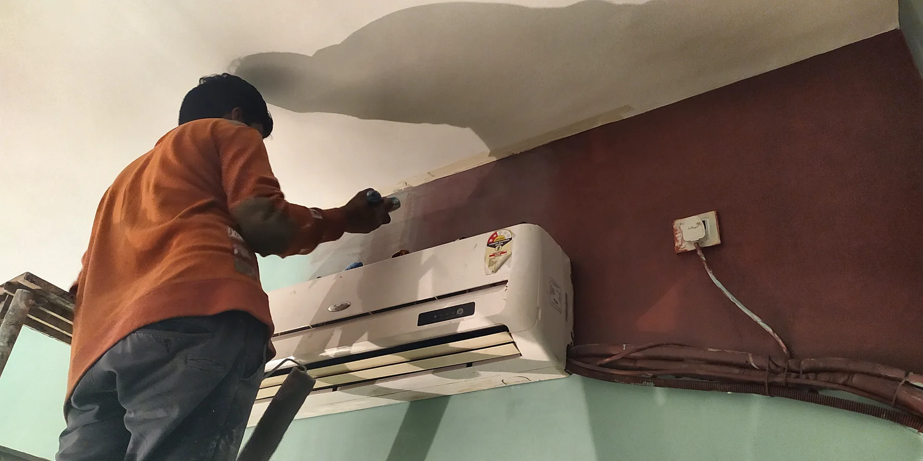 An ombre wall in the bedroom: maroon rolled on above the air-conditioner, against sage green.