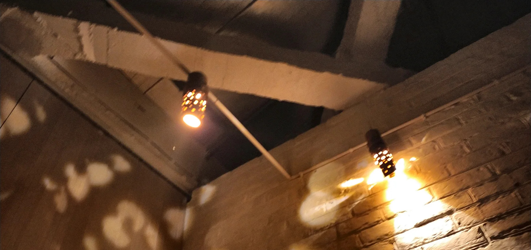 Lamps under the timber beams, throwing patterned light.